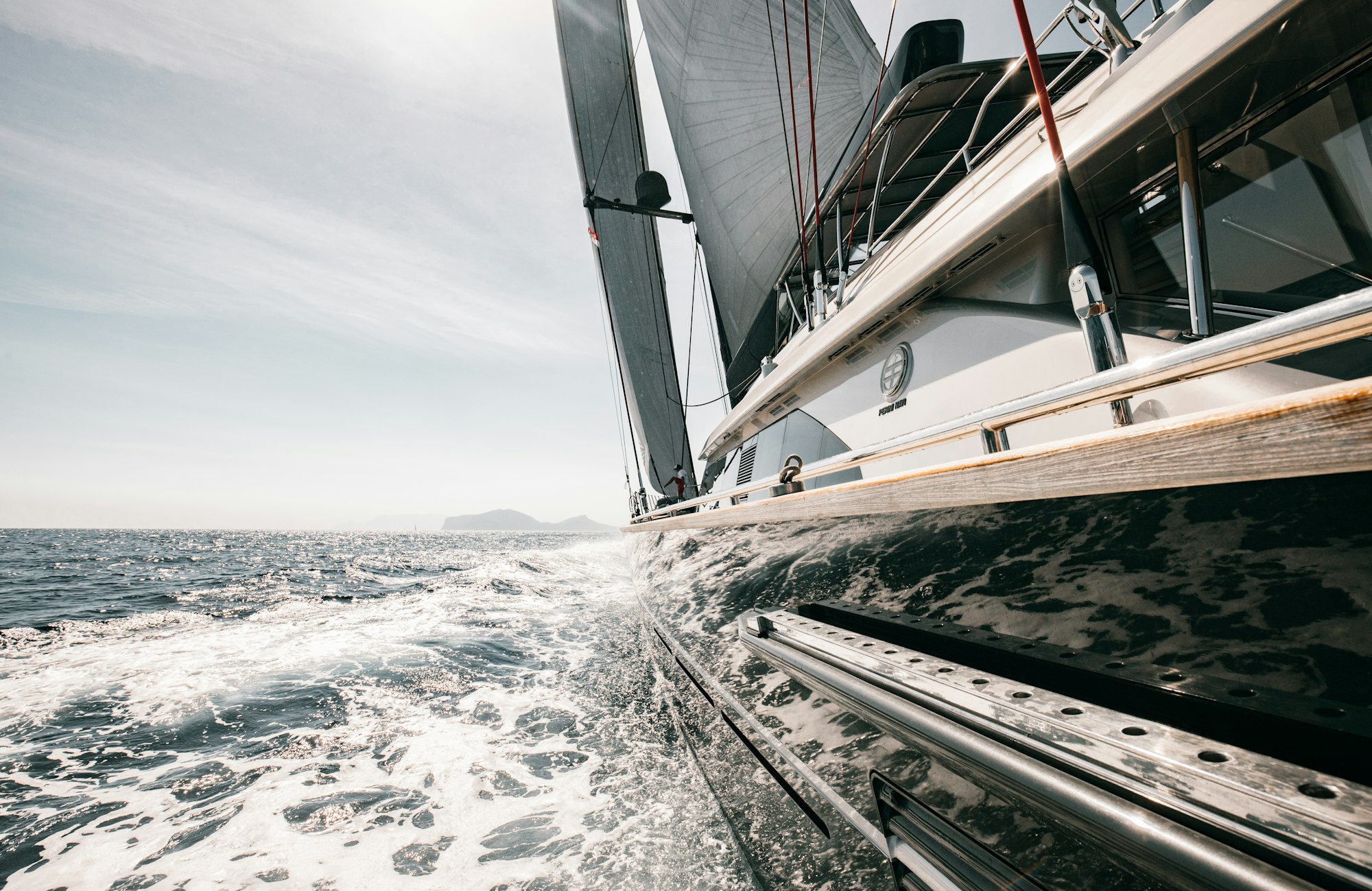 Looking down the rail of a sailing yacht under way, hull slicing through white water